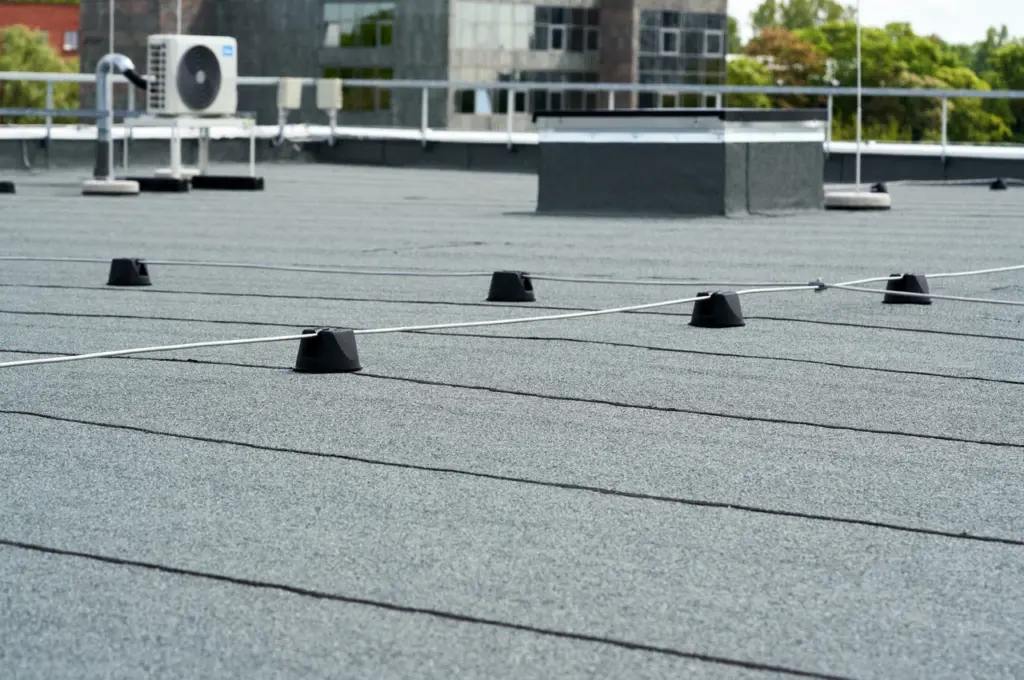 Lightning protection wires on black holder blocks installed on a grey flat roof.