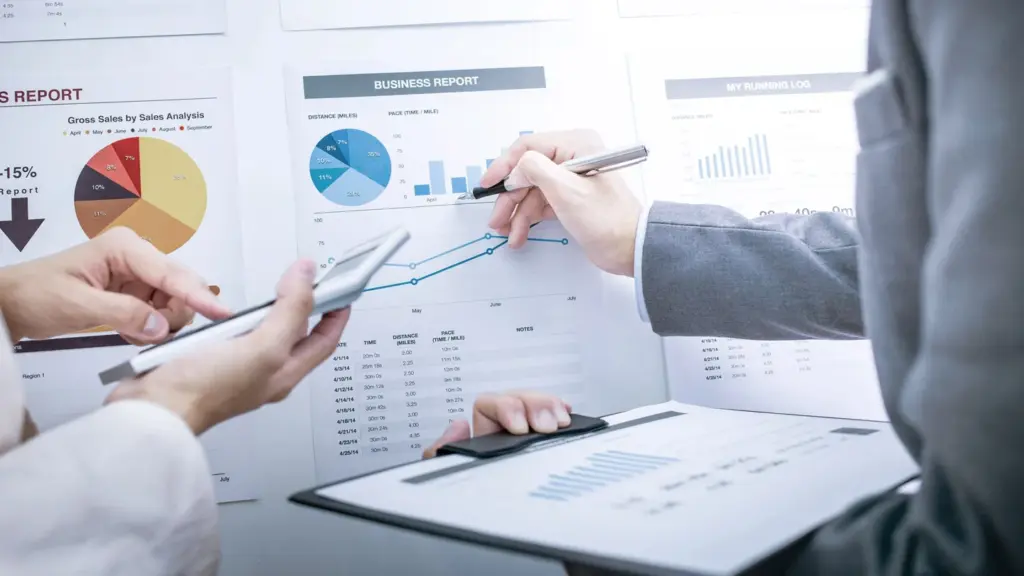 Professionals analyzing business reports with charts and graphs using a calculator and pen.