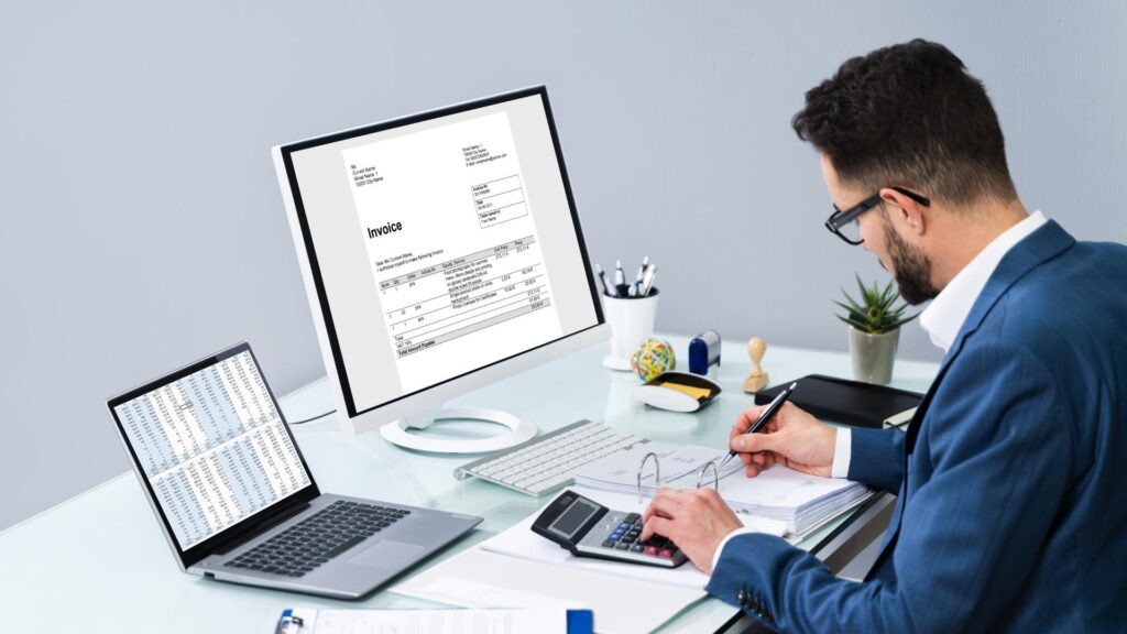 Business professional managing accounts using a computer, laptop, and calculator at a desk.