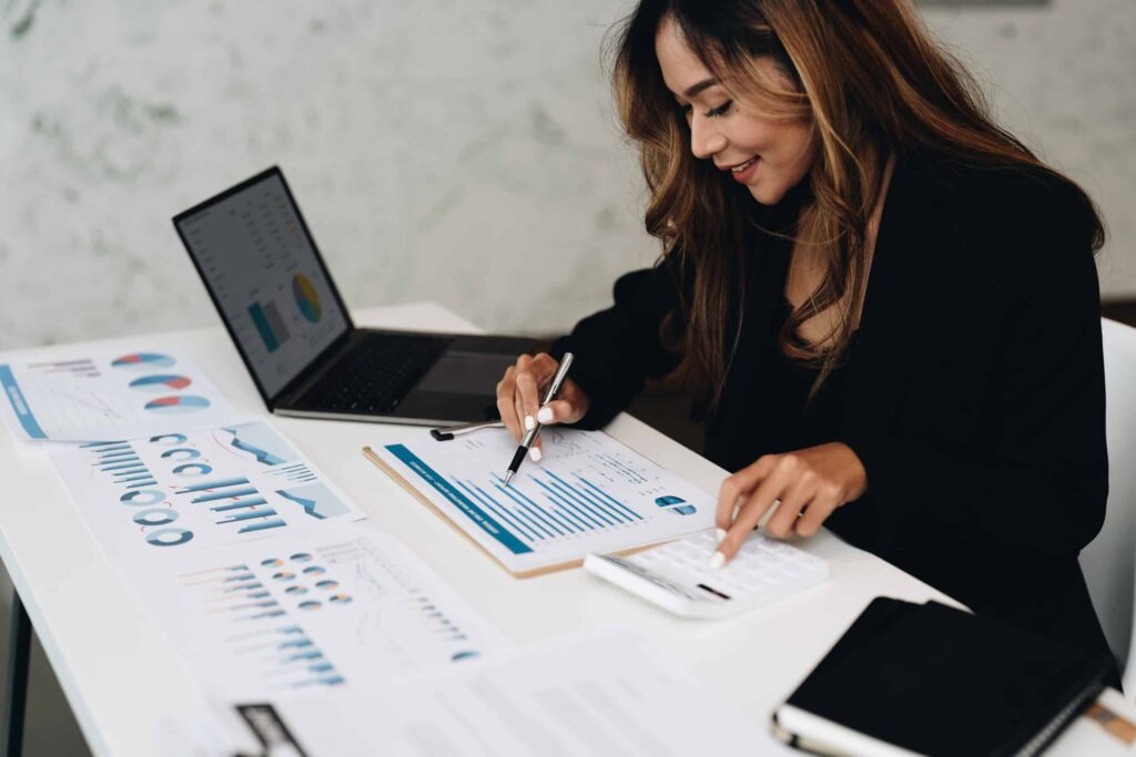 Smiling woman analyzing business data reports and charts using a calculator and pen.