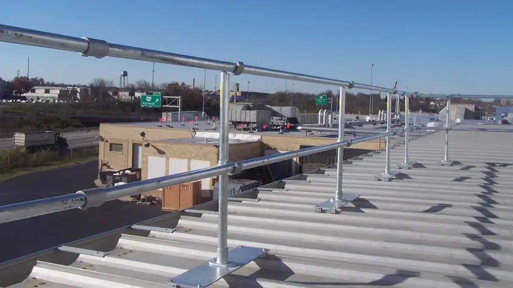 Metal safety guardrails installed on a corrugated metal rooftop overlooking a building and highway.