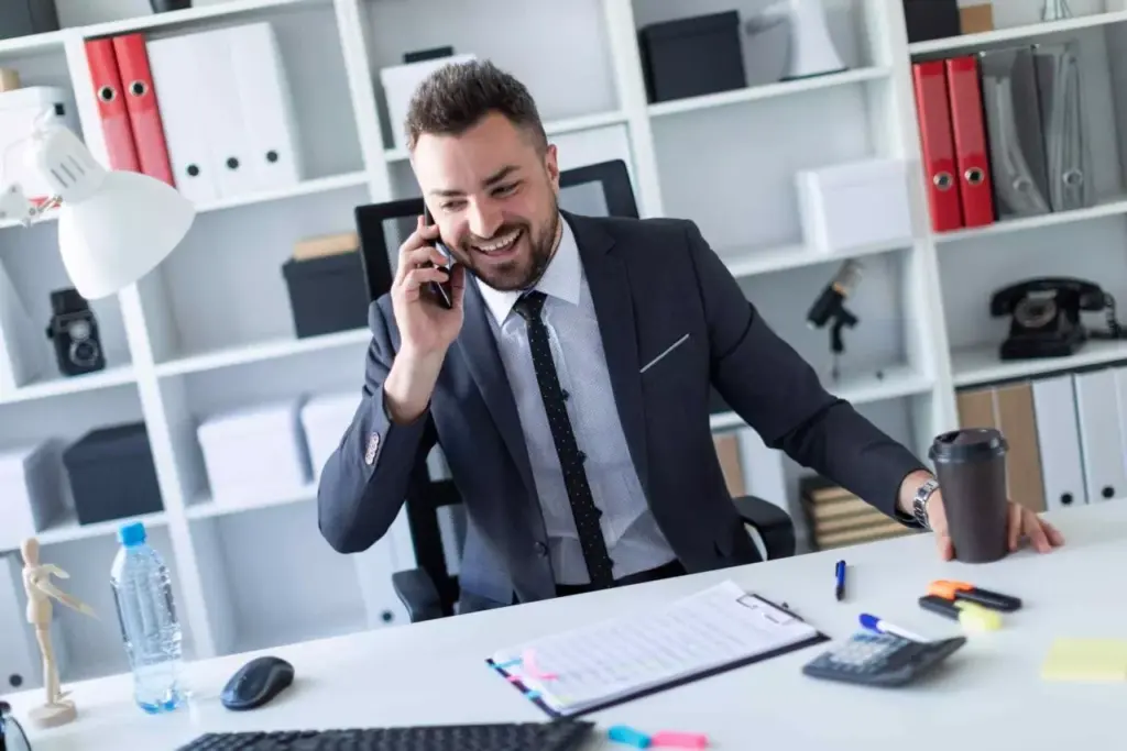 Smiling businessman in a suit talking on his cell phone at his office desk.