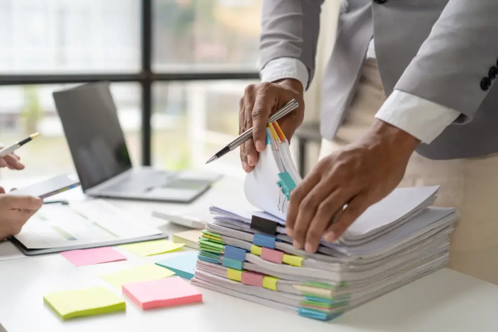 A professional organizing a thick stack of documents with colorful binder clips at an office desk.