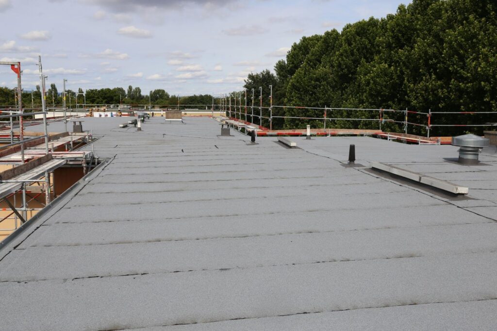 Flat gray roof with scaffolding around the perimeter and several small vents, under a partly cloudy sky.