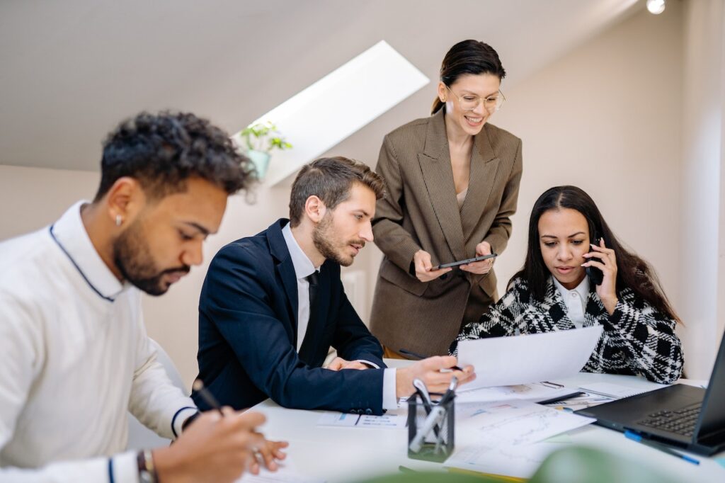 Four diverse professionals collaborating over documents and a laptop in a bright office setting.