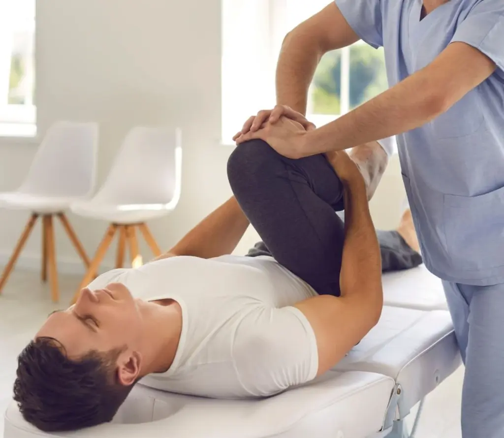 Physical therapist performing a knee stretch on a man lying on a white medical treatment table.