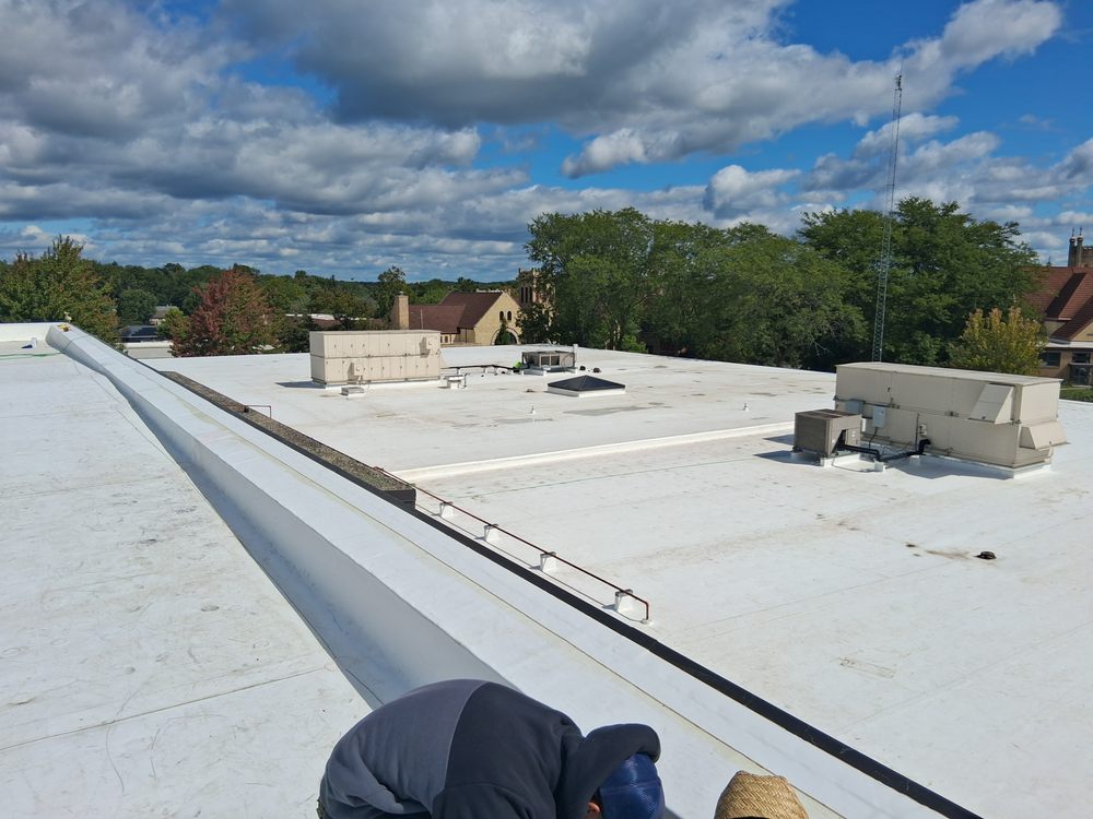 Flat white commercial roof with HVAC units under a cloudy blue sky, with trees and buildings in the background.