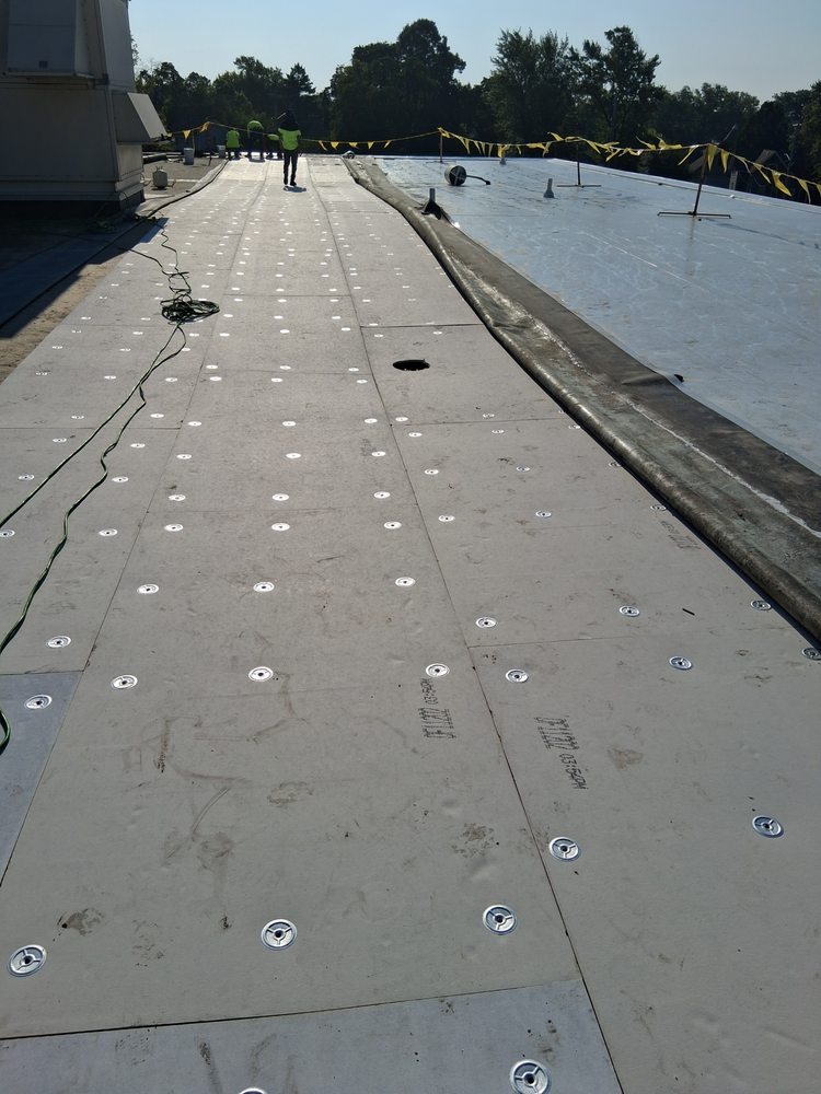 Flat roof construction site with large insulation boards secured by metal fasteners and workers in high-visibility vests.