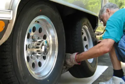 Man in a teal shirt crouching to work on the dual wheels of a vehicle.