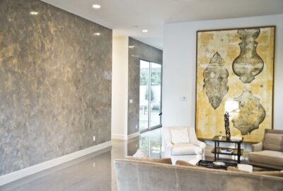 Modern living room with textured gray walls, a large yellow abstract painting, and neutral-colored seating.