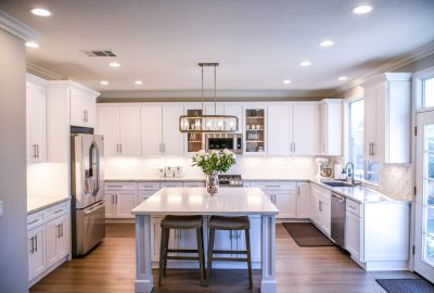 Modern kitchen with white cabinetry, a central island with brown stools, and stainless steel appliances.