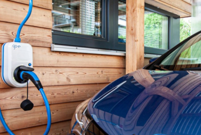 *   Image content: An electric vehicle (EV) charging station (white box with "go-e" logo) mounted on a wooden wall. A blue ch
