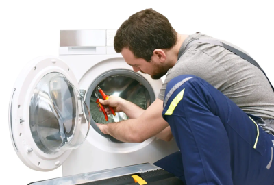 *   Image: A man in a grey t-shirt and blue work trousers (with yellow accents) is repairing a white front-loading washing ma