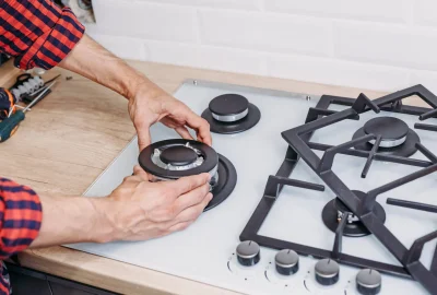 *   Image shows a person's hands working on a gas stovetop.
    *   The person is wearing a red and blue plaid shirt.
    *