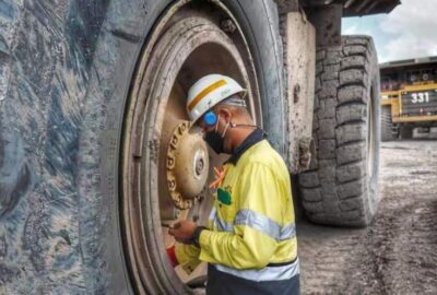 A worker in PPE inspects the hub of a massive mining truck tire.