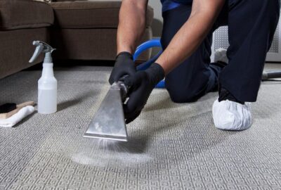 Professional cleaner using a steam vacuum wand to clean a patterned grey carpet.