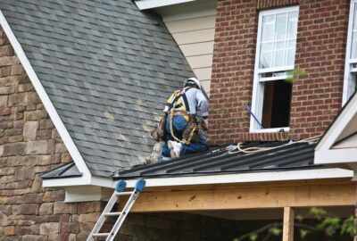 Roofer in a safety harness and tool belt repairing a residential roof.