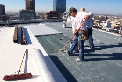 Workers sweeping a high-rise building roof against a backdrop of a city skyline.