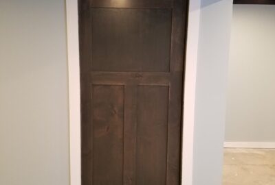 Dark wood paneled door with white trim set in a light gray wall on a concrete floor.