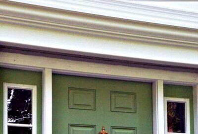 Close-up of a green front door with white trim and a pediment above.