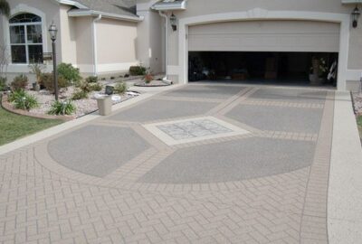 Decorative patterned concrete driveway leading to an open garage of a beige stucco home.