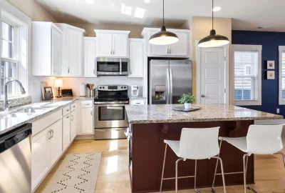 Modern kitchen with white cabinets, granite countertops, stainless steel appliances, and a large island with bar stools.