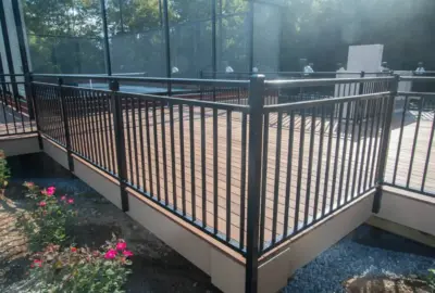 Wooden deck with black metal railings overlooking a fenced-in tennis court.