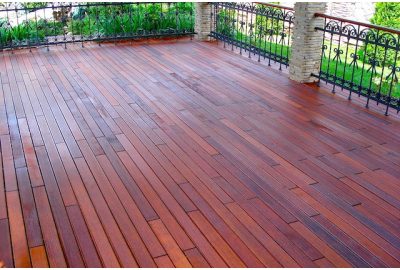 Reddish-brown polished wooden deck with black wrought iron railings and stone pillars.
