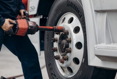 Mechanic using a heavy-duty pneumatic impact wrench on a truck wheel lug nut.