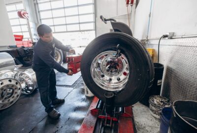 Mechanic operating a tire changing machine to service a large truck wheel in a workshop.