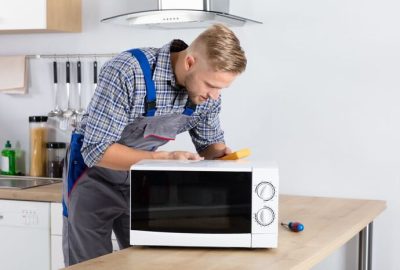 *   Image content: A man in blue and grey overalls (technician/repairman) is working on a white microwave oven.
    *   Setti