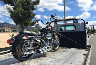 *   Image content: A black cruiser-style motorcycle (looks like a Harley-Davidson) secured with a strap on the flatbed of a w