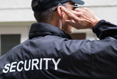Security guard in black uniform and cap adjusting a communication earpiece.