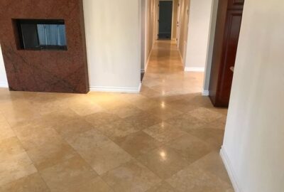 Wide shot of a modern interior featuring polished beige tile flooring, a red marble fireplace, and a long hallway.