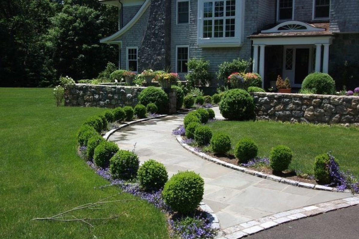 A beautifully landscaped pathway leading to a home, bordered by greenery and decorative features.