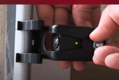 Hands mounting a small black sensor with a green indicator light to a metal pole.