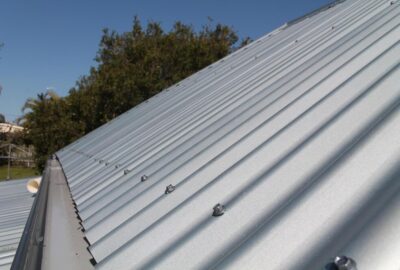 Close-up of a silver corrugated metal roof with mounting screws against a clear blue sky.