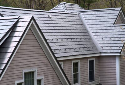 Close-up of a house with light gray metal shingle roofing and snow guards installed on the sloped roof sections.