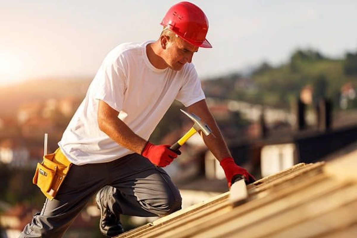 *   Image: A construction worker wearing a red hard hat, white t-shirt, grey pants, red gloves, and a tool belt. He is kneeli