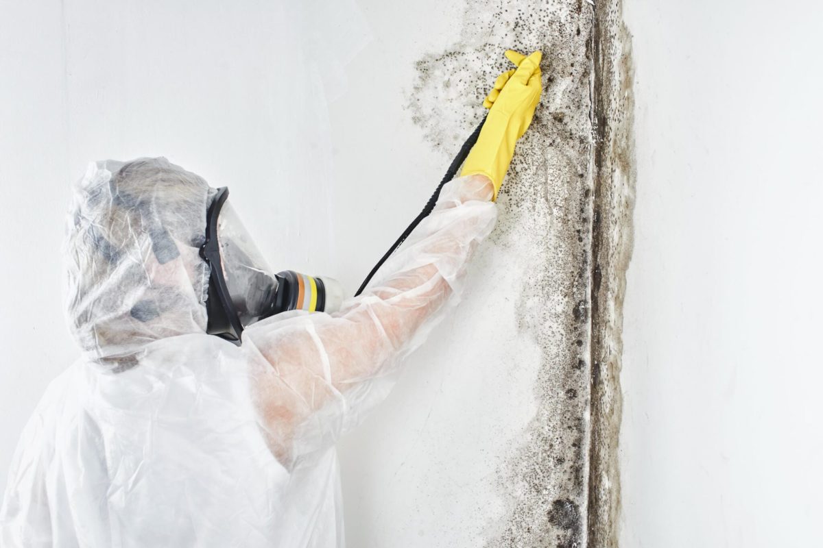 *   Image shows a person in full protective gear (white hazmat suit, respirator mask, yellow gloves).
    *   The person is u