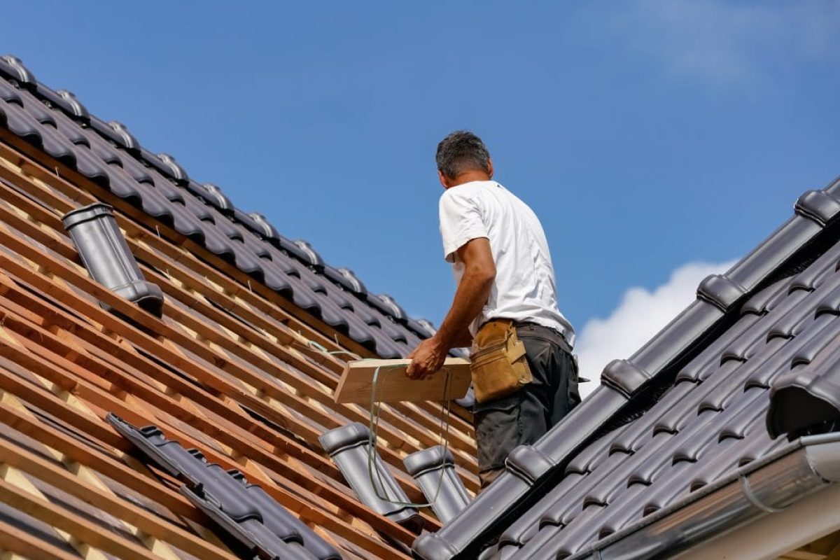 *   Image: A man in a white t-shirt and work pants with a tool belt is working on a roof.
    *   Action: He is installing or