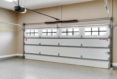 White sectional garage door with top windows and an automatic overhead opener in a garage with a gray epoxy floor.
