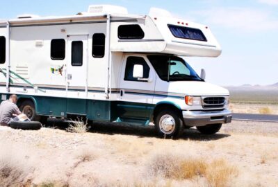 A man works on a white and green motorhome parked on the side of a desert road.