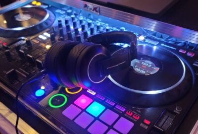 Black headphones resting on a professional DJ controller with glowing colorful buttons and jog wheels.