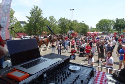DJ setup overlooking a crowd and horse-drawn carriages at an outdoor community event.