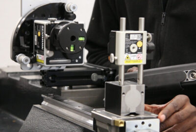 Person adjusting Renishaw precision laser measurement equipment on a metal workbench.