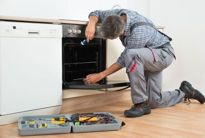*   Image: A man in work clothes (plaid shirt, grey overalls) is kneeling in a kitchen.
    *   Action: He is repairing an ov