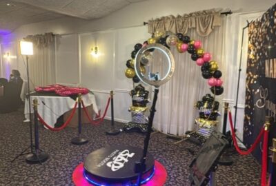 360 photo booth setup with a rotating ring light and a black, gold, and pink balloon arch backdrop.