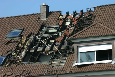 A brown tiled roof with severe fire damage, exposing charred wooden beams and missing tiles.