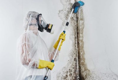 *   Image content: A person wearing full protective gear (white hazmat suit, respirator mask, yellow gloves) scrubbing a larg